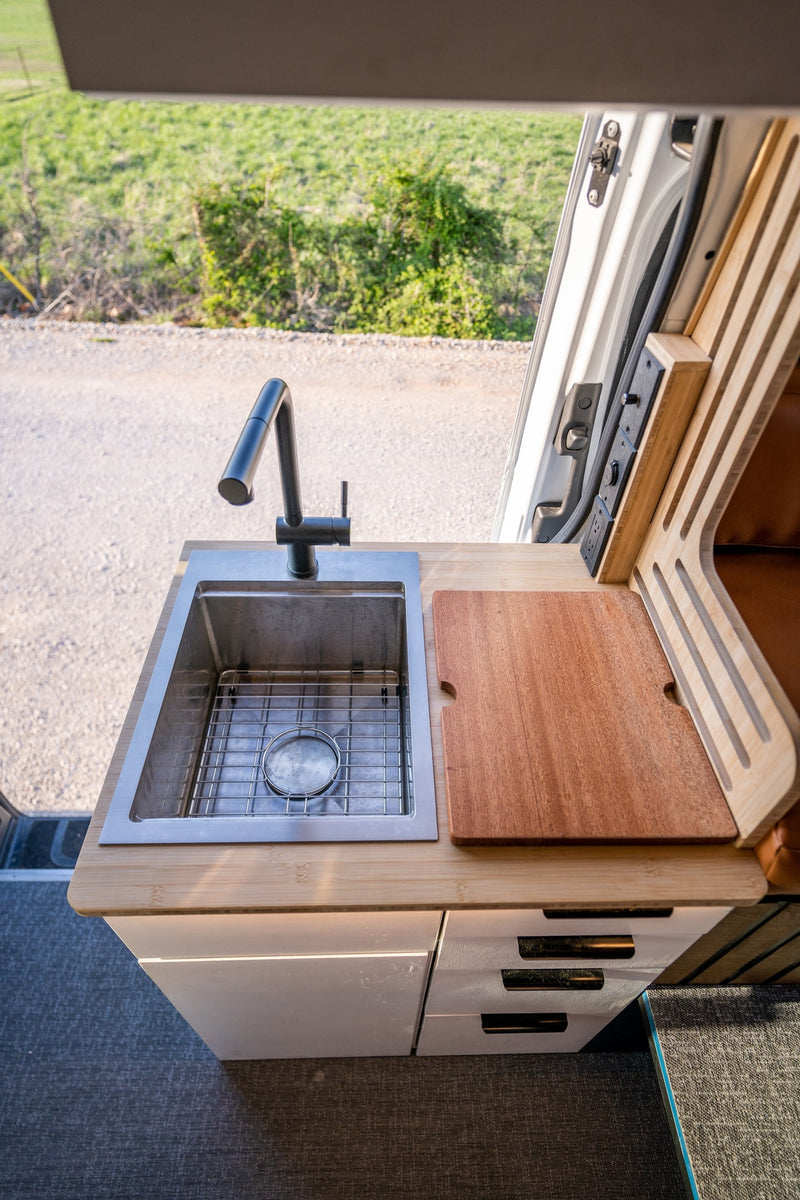Inside an rv rental: a modern kitchenette with sink, faucet, cutting board, and cabinetry, offering an outdoor view. — photo 19