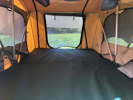 Interior of an RV rental: a comfy sleeping area with a mattress and scenic window view of green nature, ideal for outdoor travel.