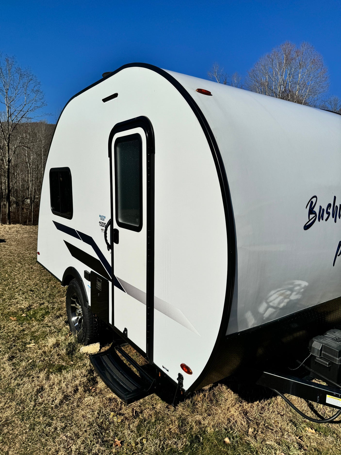 Sleek white travel trailer, an ideal rv rental camper, parked on dry grass under a bright blue sky with distant bare trees.