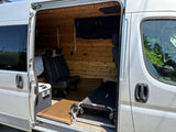 Inside this silver RV rental, wood paneling, black seats, a cooler, sleeping pad, and a cot offer adventure-ready comfort.