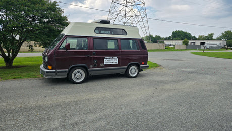 Maroon VW T3 pop-top camper van, a perfect RV rental option. Parked on asphalt with distinctive multi-spoke wheels.