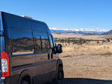 RV rental van on a gravel road overlooking a vast landscape with majestic snow-capped mountains.