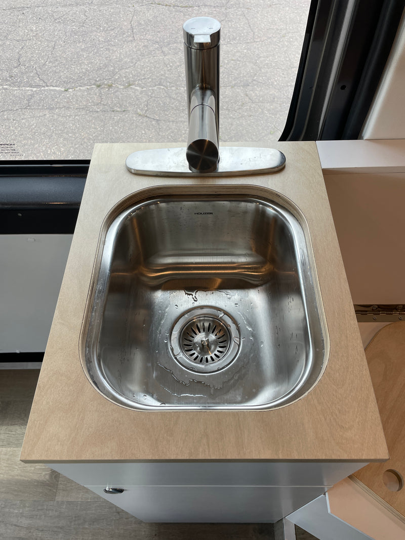 Modern sink and faucet on a wood countertop over a gray cabinet, seen inside an RV rental. Paved ground visible outside. — photo 13