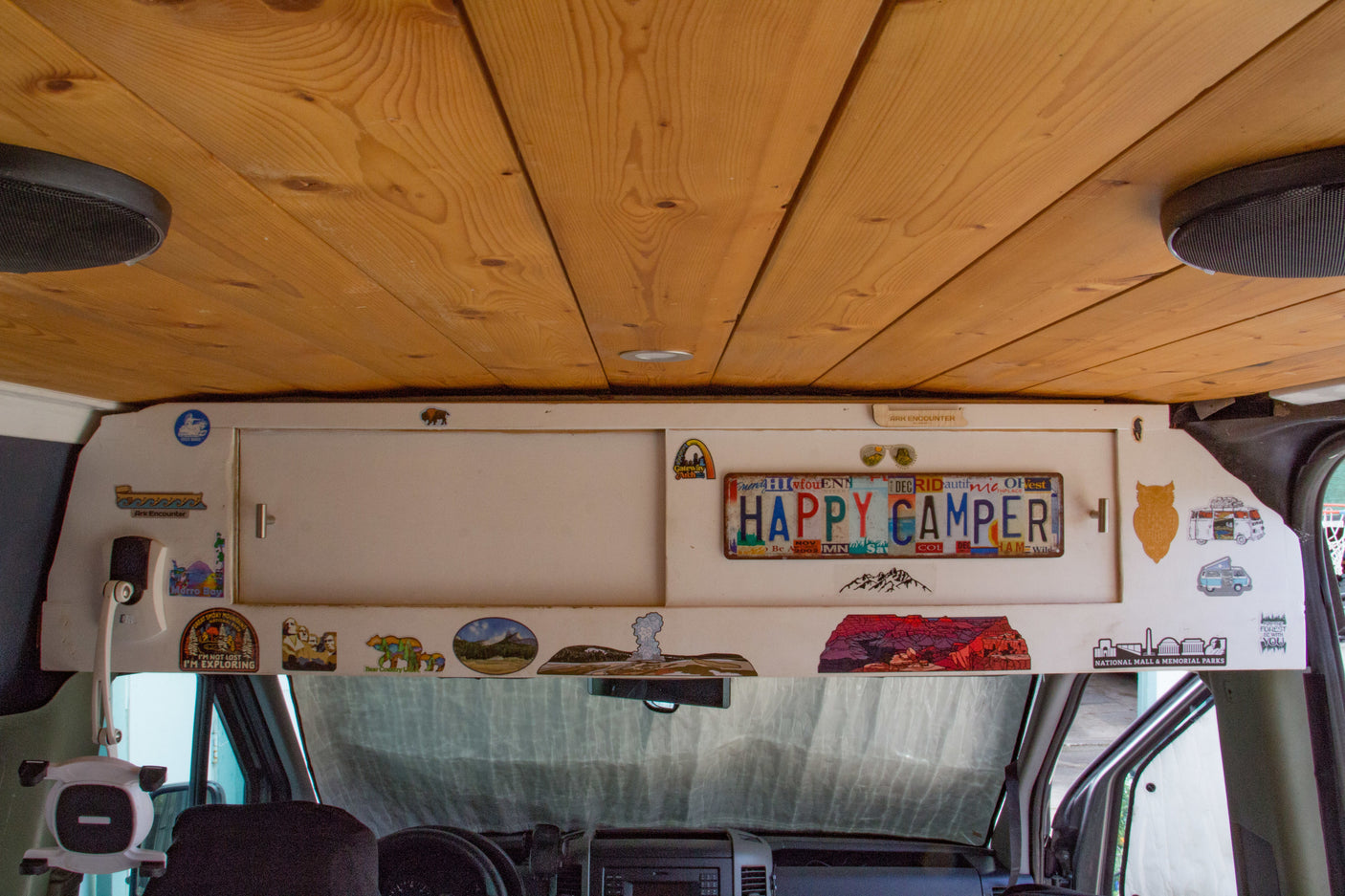 RV rental interior: wooden ceiling, custom overhead storage with travel stickers and a "HAPPY CAMPER" license plate.