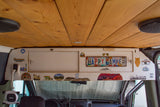 RV rental interior: wooden ceiling, custom overhead storage with travel stickers and a "HAPPY CAMPER" license plate.