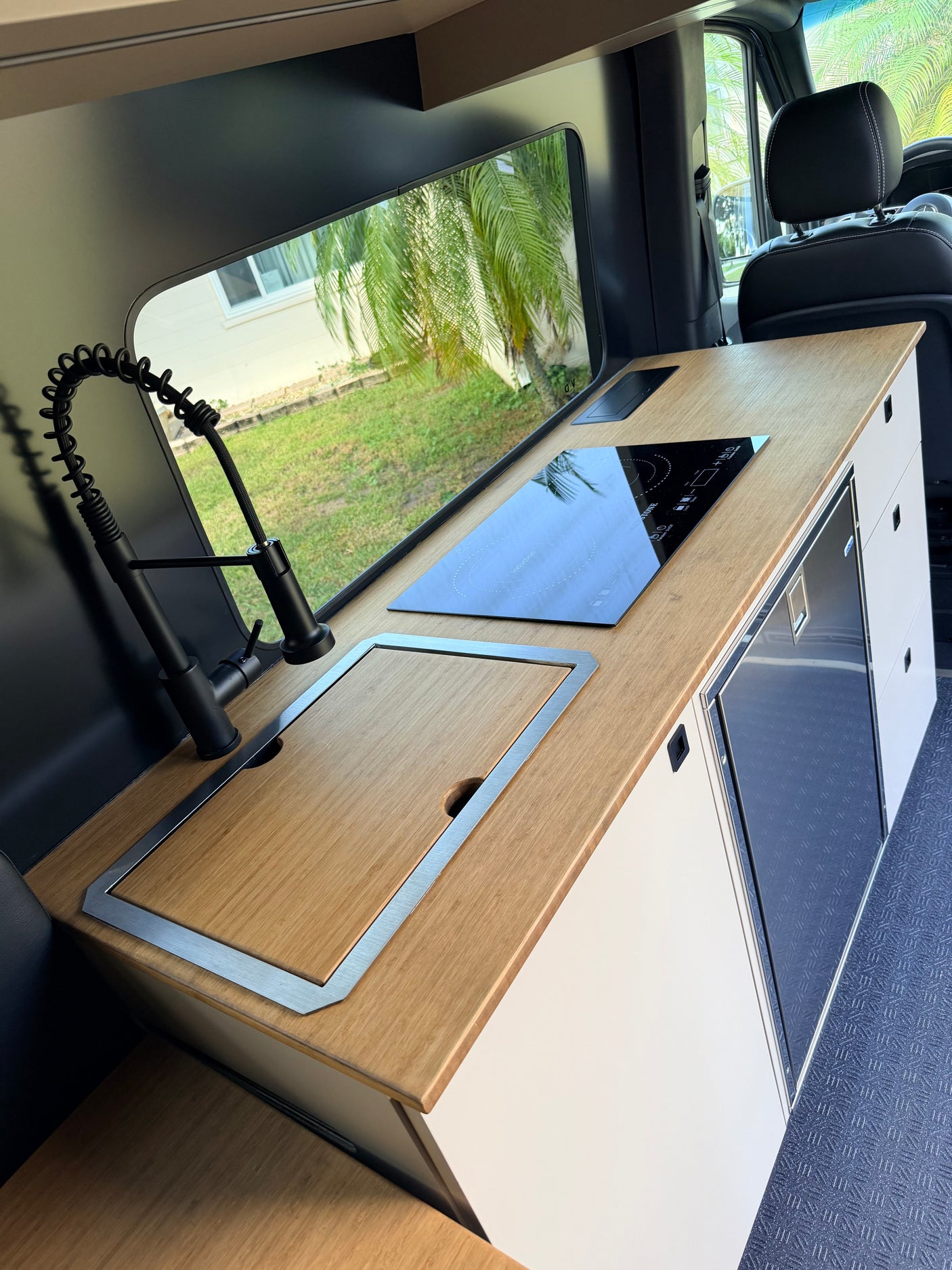 Modern camper van kitchen in an **rv rental**, featuring an induction cooktop, covered sink, and fridge for comfortable trips.