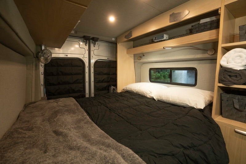 Cozy RV rental bedroom with black bedding, a fan, and smart storage shelves for comfortable travel. — photo 6
