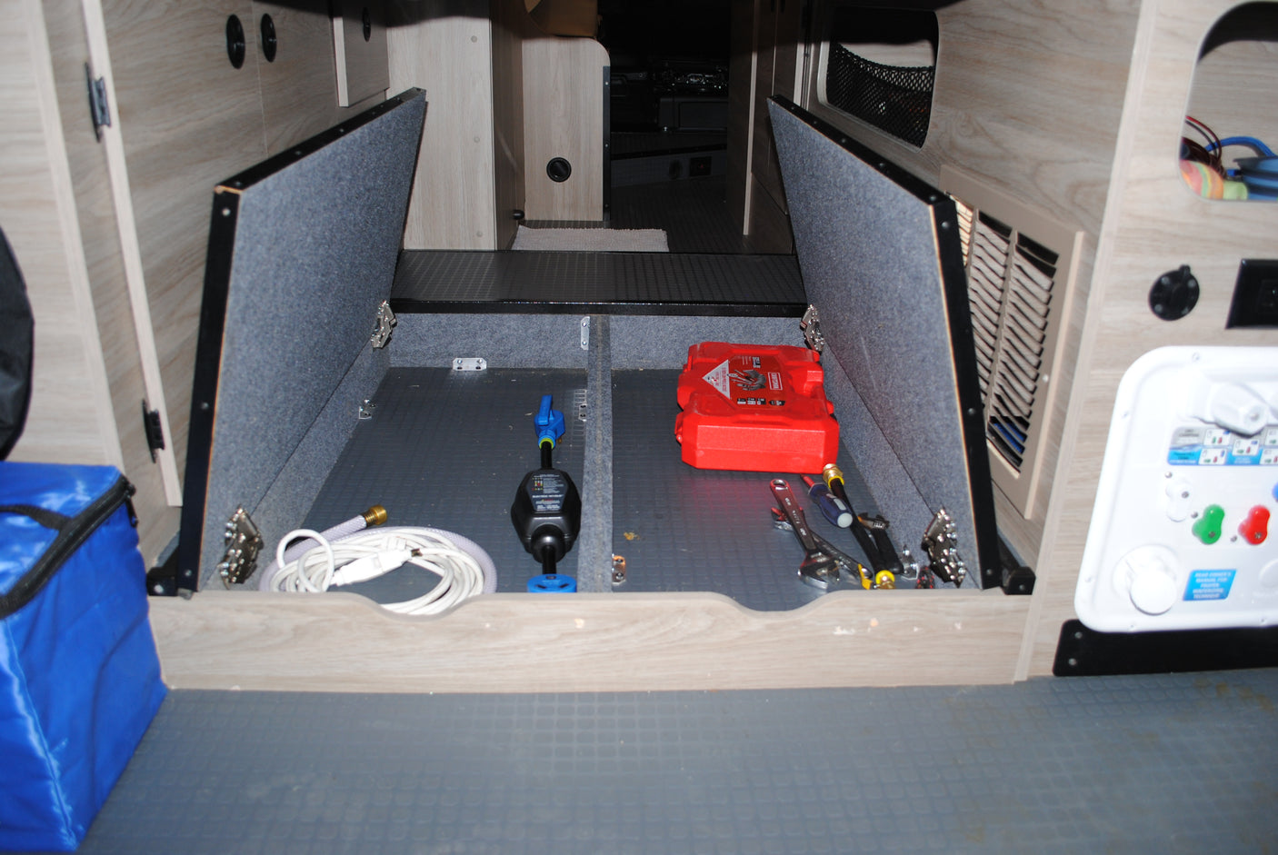 Inside an RV rental: organized under-floor storage with maintenance tools, water hose, and power utility panel.