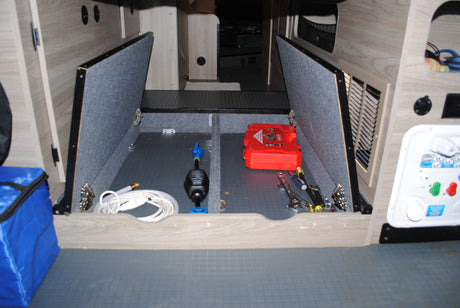 Inside an RV rental: organized under-floor storage with maintenance tools, water hose, and power utility panel.