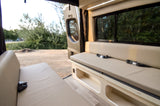 Spacious RV rental interior with light-colored bench seating, seatbelts, and built-in storage. Scenic outdoor view.