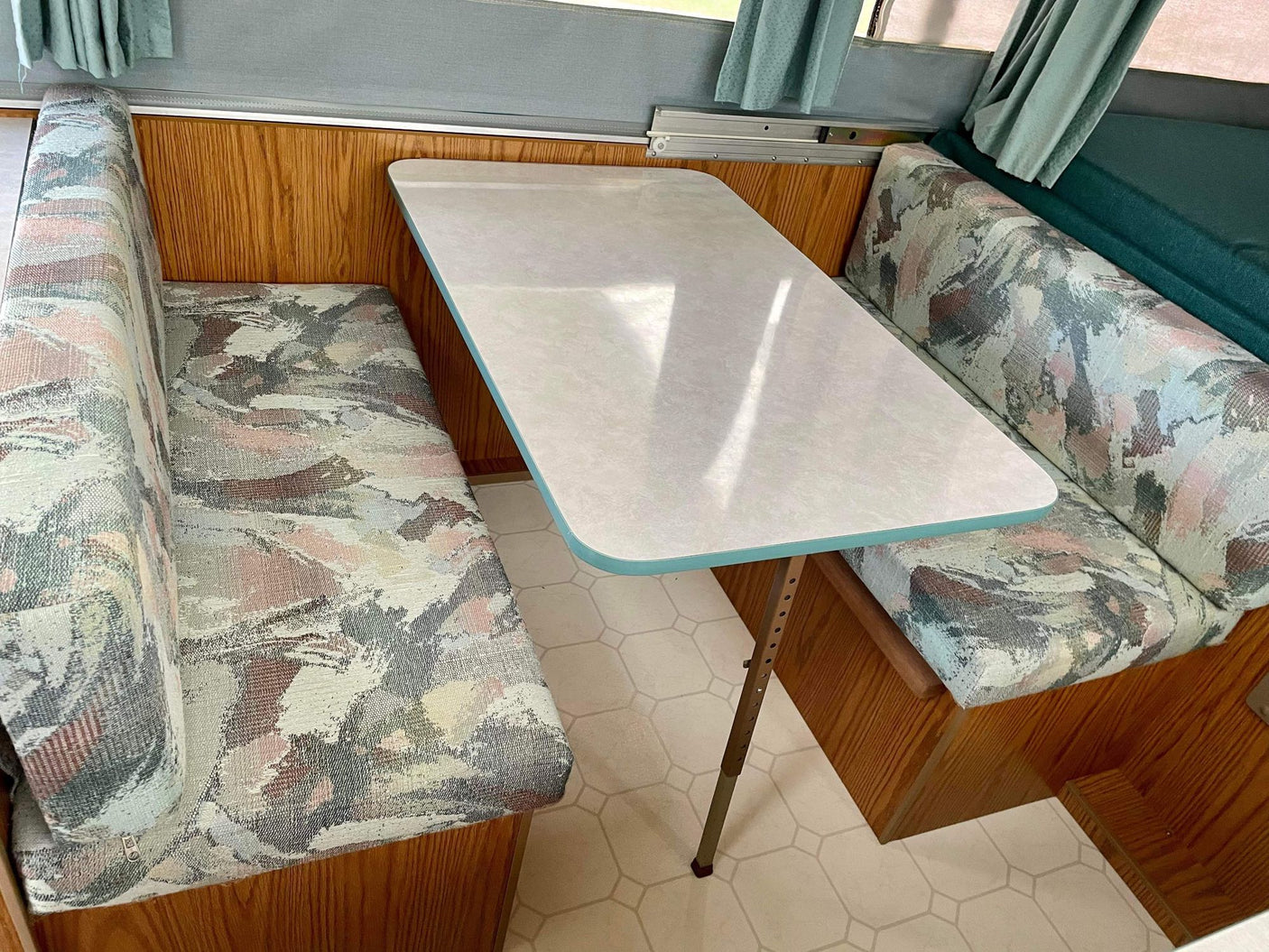 RV rental interior: A camper's dinette area features a light table, patterned benches, and wood paneling.