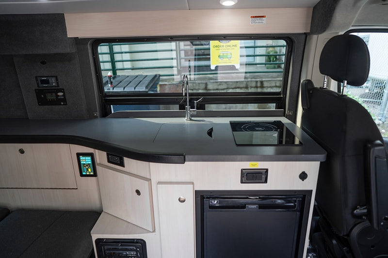 RV rental interior: A modern camper kitchen featuring a sink, induction cooktop, fridge, and wall-mounted controls. — photo 9
