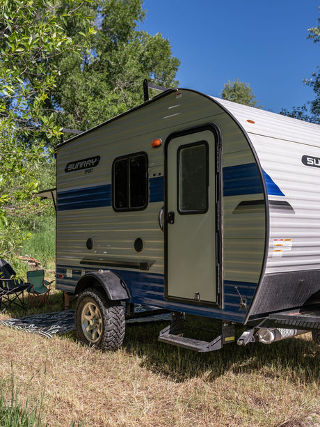 SunRay Sport RV rental trailer parked in a sunny, tree-lined campsite. Ready for your next outdoor adventure.