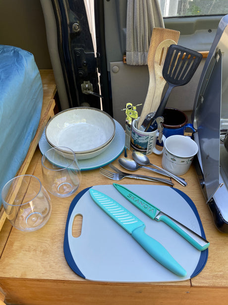 RV rental kitchen: dishes, glasses, cooking utensils & knives on a cutting board, ready for adventure meals.
