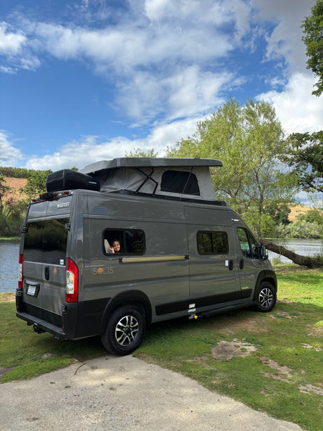 Winnebago Solis RV rental parked riverside, with a happy child waving from the window.