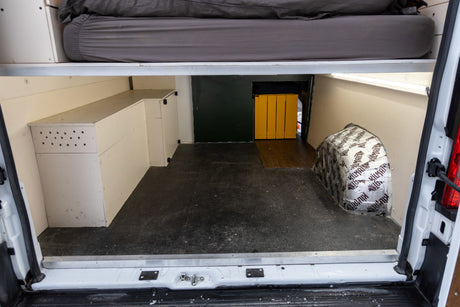 Inside an RV rental campervan: organized under-bed storage, custom cabinetry, and insulated wheel well for efficient travel setup.