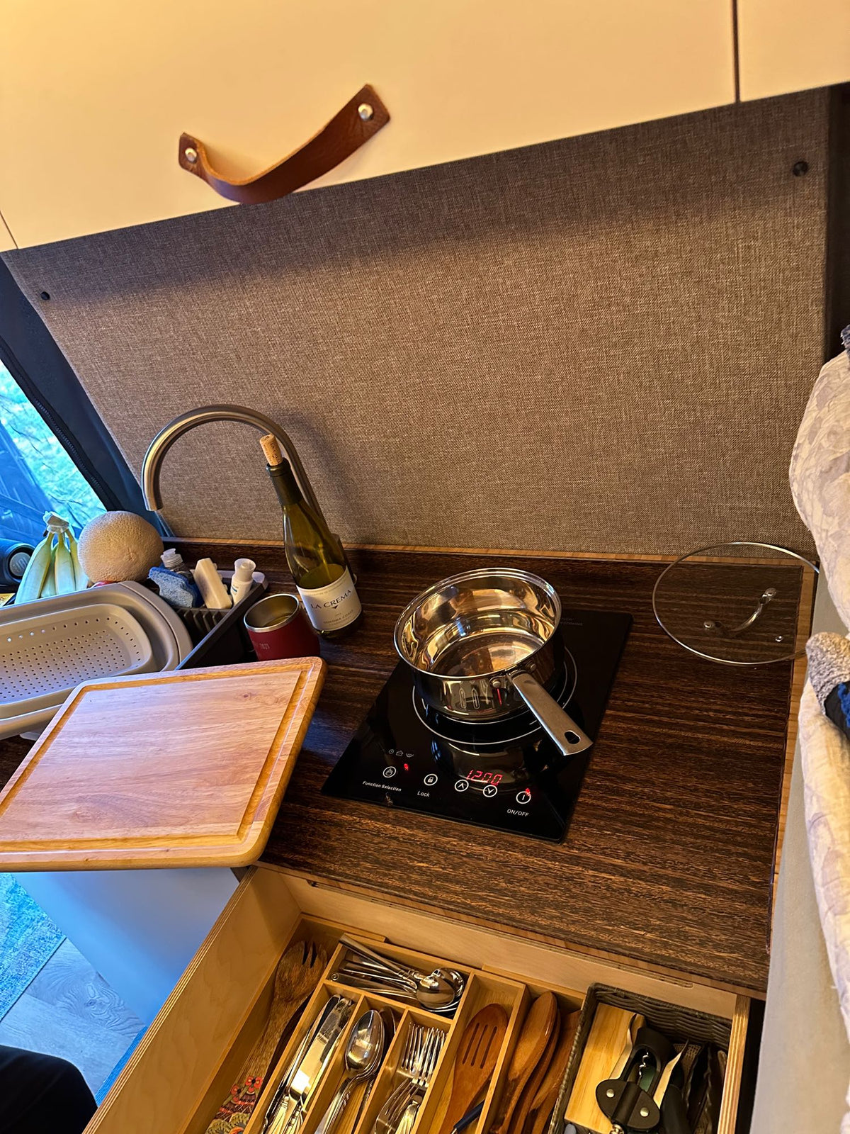 Compact RV rental kitchen with sink, induction cooktop, cutting board, and organized utensil drawer. — photo 8
