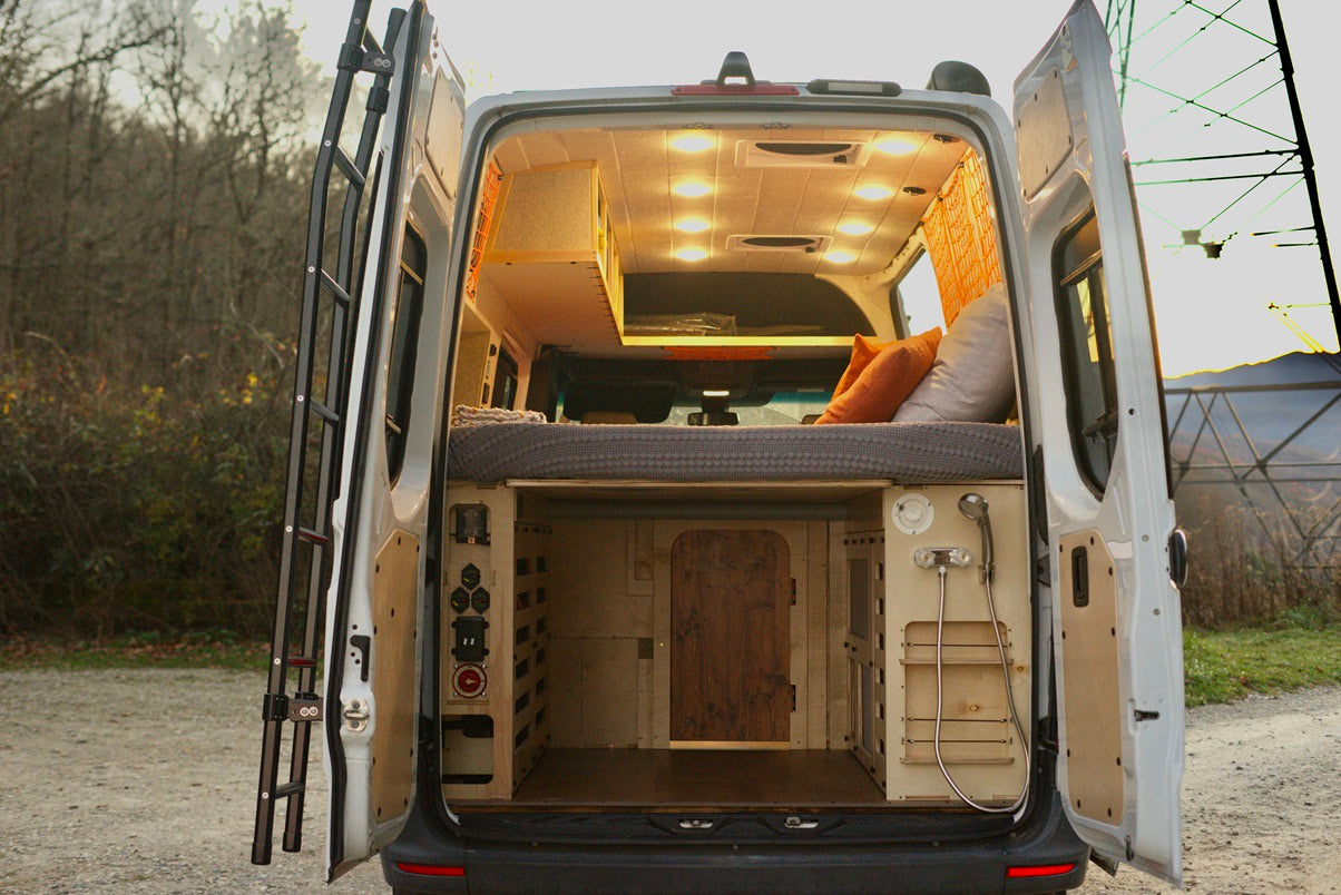 Explore this RV rental camper van. Rear view shows a bed, storage area below, and an outdoor shower, ideal for mobile adventures.