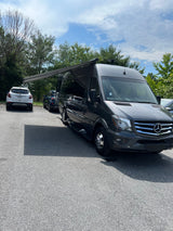 A dark grey Mercedes Sprinter camper van, an ideal RV rental, with its awning extended in a sunny parking lot.