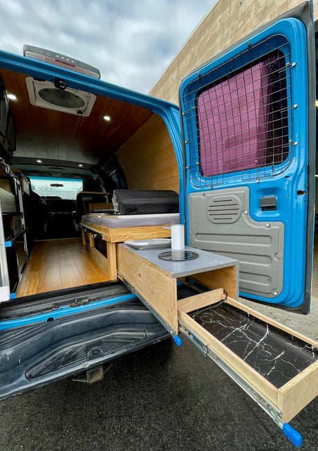 RV rental-ready blue camper van interior featuring a pull-out kitchen, bed, and stylish wood-paneled walls.