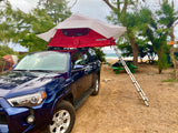 Beachside RV rental: blue SUV with rooftop tent deployed for sandy camping by the ocean.