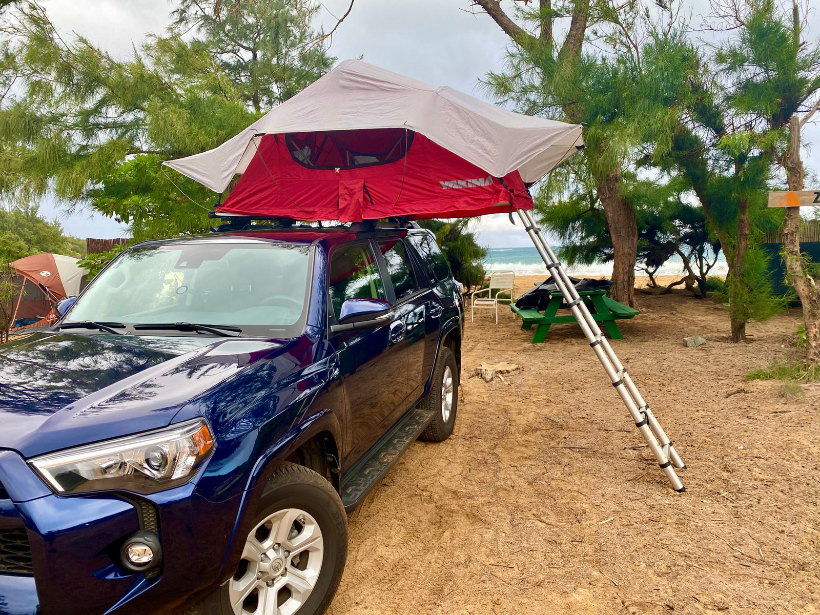 Beachside RV rental: blue SUV with rooftop tent deployed for sandy camping by the ocean.
