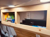RV rental amenities: a wooden built-in shelf displaying a Blokus game, a USB outlet, and a Foxnovo soundbar for entertainment.