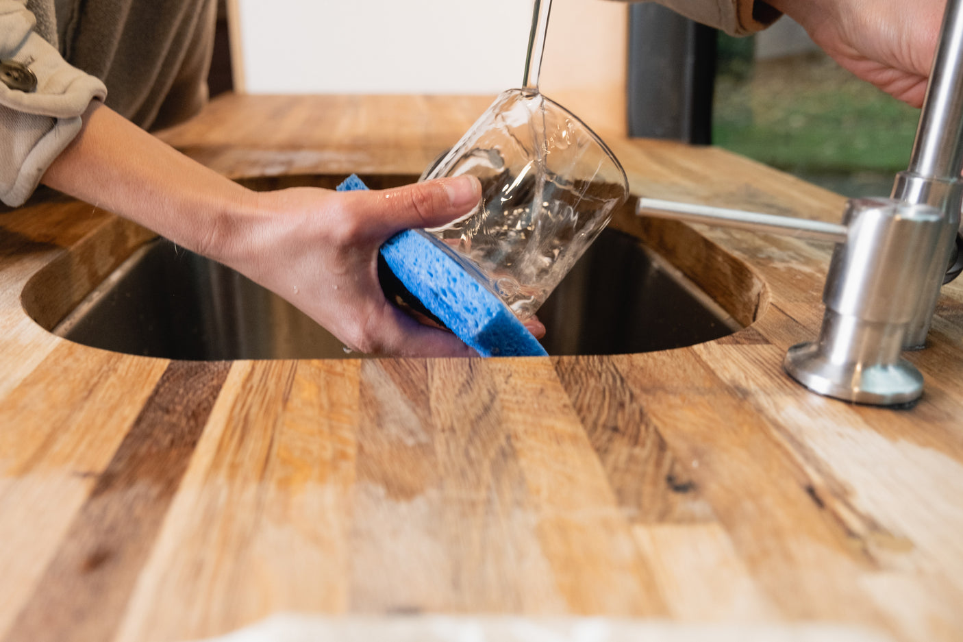 Hands wash a glass in a compact RV rental kitchen sink. Enjoy convenient amenities on your next adventure!