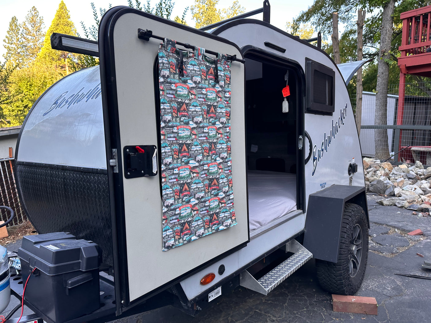 This compact Bushwhacker RV rental camper trailer with its door open reveals a cozy bed, perfect for your outdoor adventures.