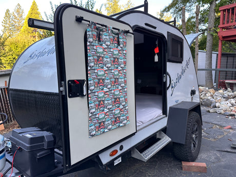 This compact Bushwhacker RV rental camper trailer with its door open reveals a cozy bed, perfect for your outdoor adventures.