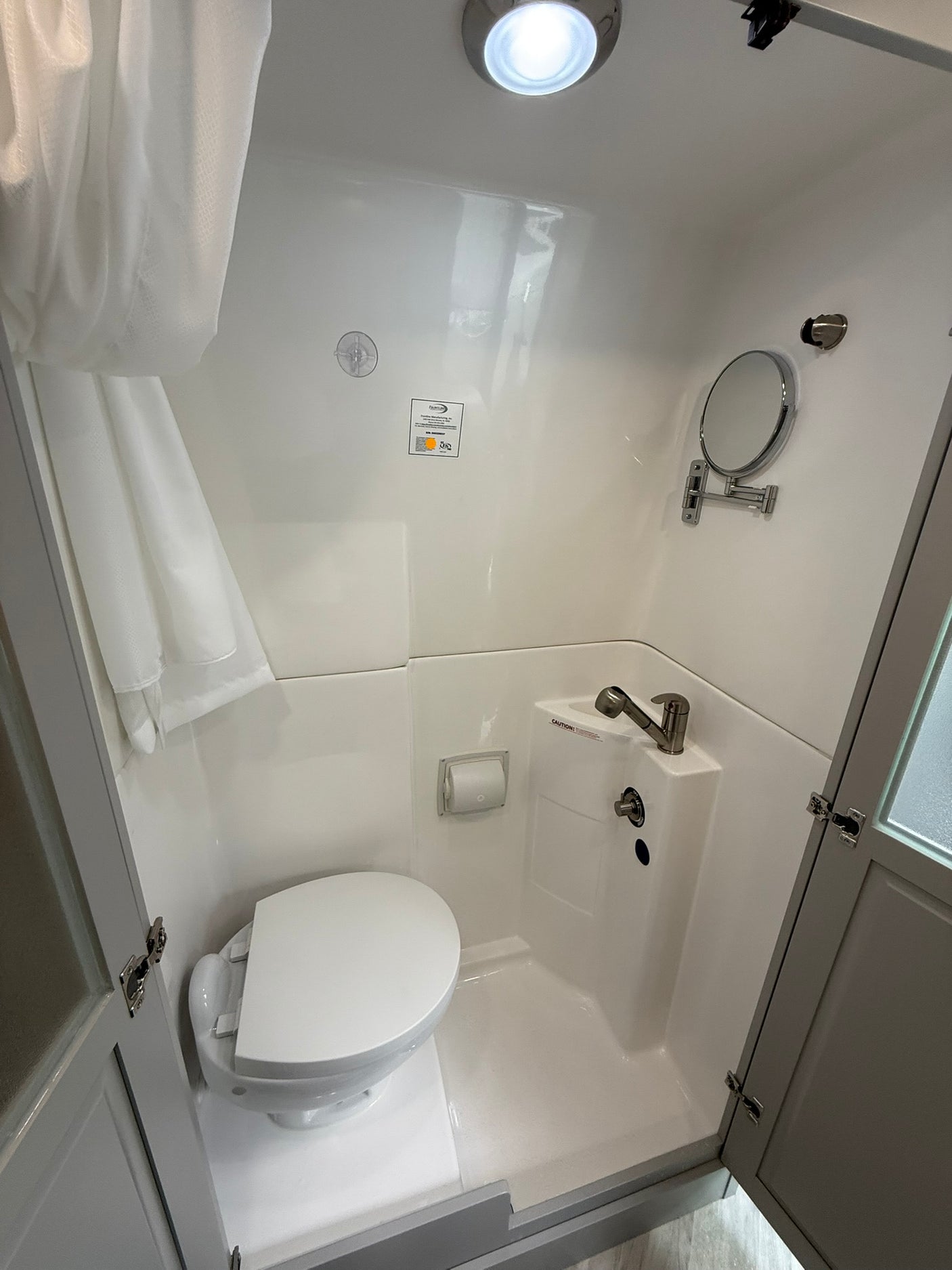 Compact RV rental's white bathroom features a toilet, integrated sink/shower combo, mirror, and bright overhead light.