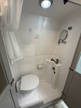 Compact RV rental's white bathroom features a toilet, integrated sink/shower combo, mirror, and bright overhead light.