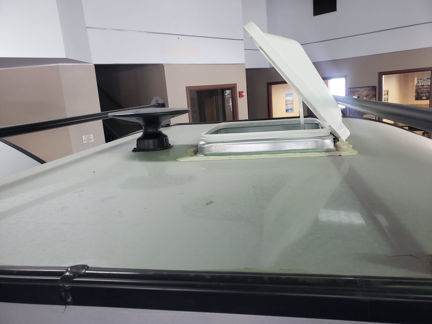 Discover features of an RV rental: close-up of an open rooftop skylight, antenna base, and roof rails on display.
