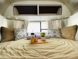 Experience a cozy RV rental: bedroom with polished walls, plush pillows, and a French press breakfast in bed.