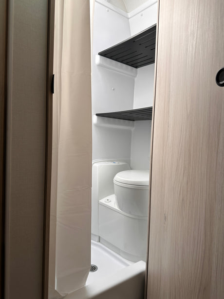 RV rental: Compact bathroom with white toilet, shower pan, black shelves, and a beige shower curtain.