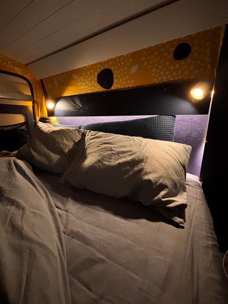 Cozy RV rental sleeping area features a grey bed, warm lights, and yellow patterned wall fabric for comfort.