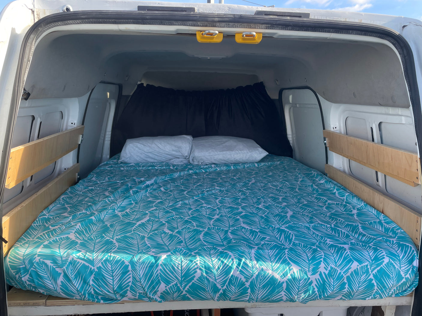 Inside an RV rental: a comfy bed with teal leaf sheets and pillows, ready for van life adventures.