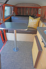 Inside a classic camper van RV rental. Features a portable table, bench seating with a pillow, and a compact kitchen area.