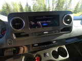 Mercedes-Benz RV rental dashboard: infotainment screen displays a warning. Controls, air vents, and outdoor trees are visible.