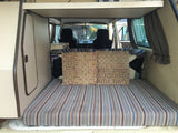 Inside an rv rental: View from the rear of a camper van, showing a striped bed, decorative pillows, and front seats.