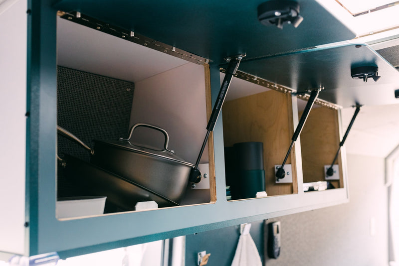 Spacious overhead storage in an RV rental, featuring open cabinets with gas struts, a pot, and kitchen essentials. — photo 7