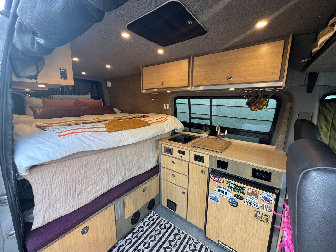 Cozy RV rental interior with a comfortable bed, bamboo kitchenette, overhead cabinets, and built-in fridge. — photo 9
