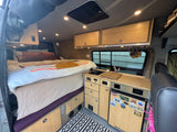 Cozy RV rental interior with a comfortable bed, bamboo kitchenette, overhead cabinets, and built-in fridge.