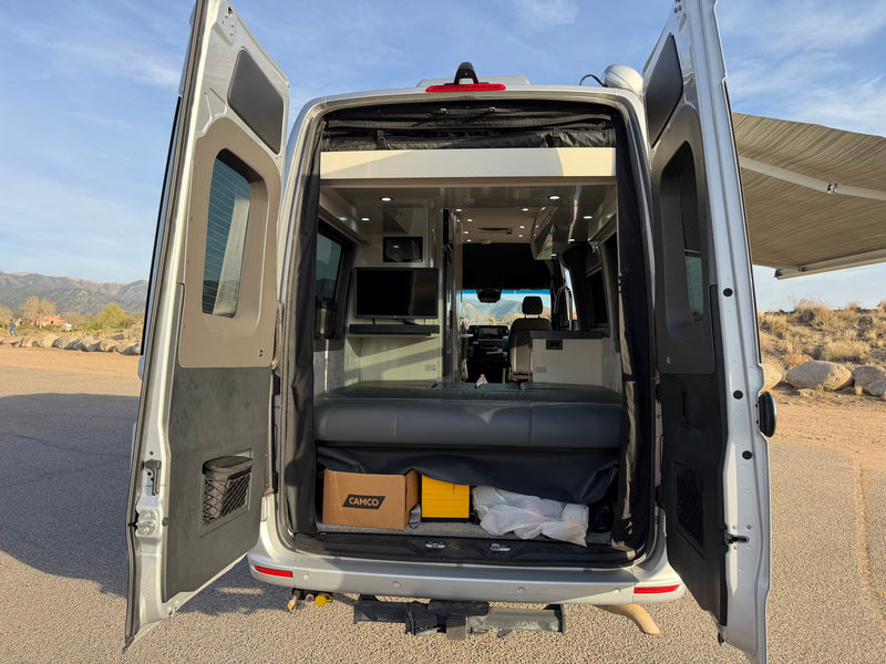 Open rear doors of a silver RV rental, showing the interior with a bed, TV, and storage, ready for adventure. — photo 18