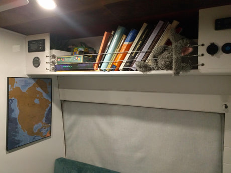 RV rental interior showing a well-organized overhead shelf with books, board games, and controls. Adventure awaits!