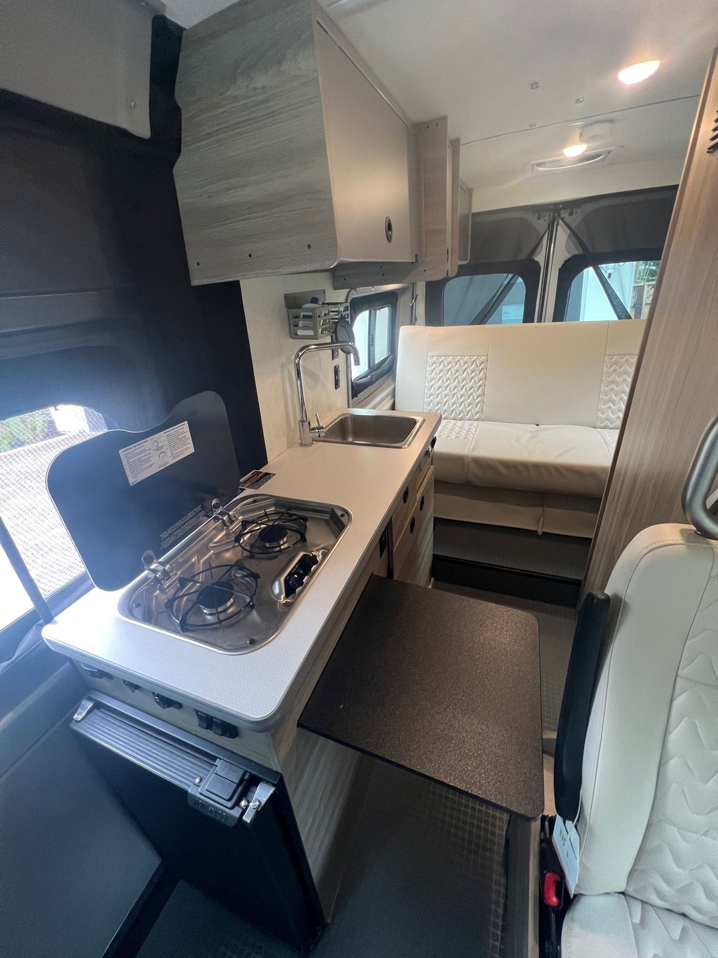 Inside this modern RV rental: a compact kitchen with stove, sink & fridge, plus comfy bench seating & fold-out table.