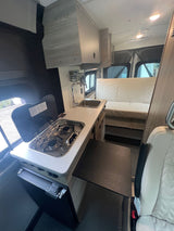 Inside this modern RV rental: a compact kitchen with stove, sink & fridge, plus comfy bench seating & fold-out table.