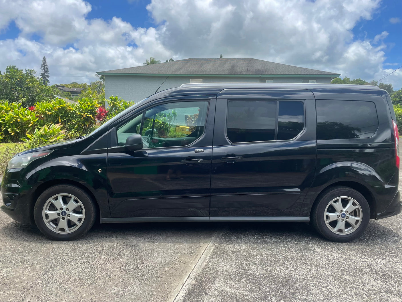 Side view of a black Ford Transit Connect van parked on an asphalt driveway. A practical choice for your rv rental needs.