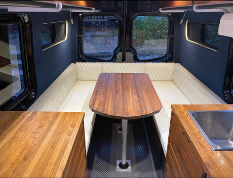 Inside this premium rv rental, a camper van's elegant interior boasts a central wooden dining table, U-shaped seating, and kitchen.