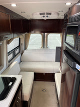 Inside a luxurious RV rental: sleek white seating, dark wood cabinets, kitchenette, microwave & fridge. Ideal for road trips.